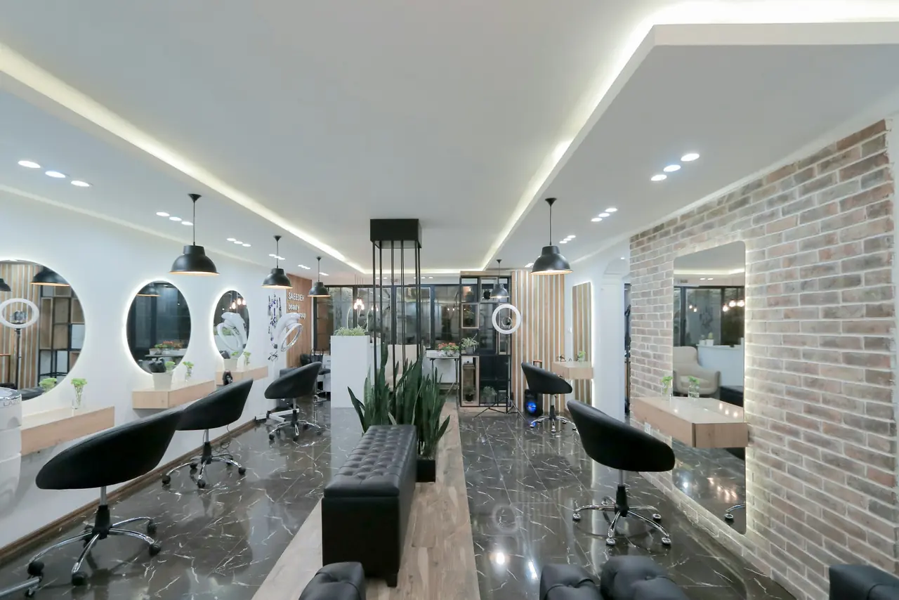 Salon de coiffure moderne : miroirs ronds éclairés, fauteuils noirs et mur de briques
