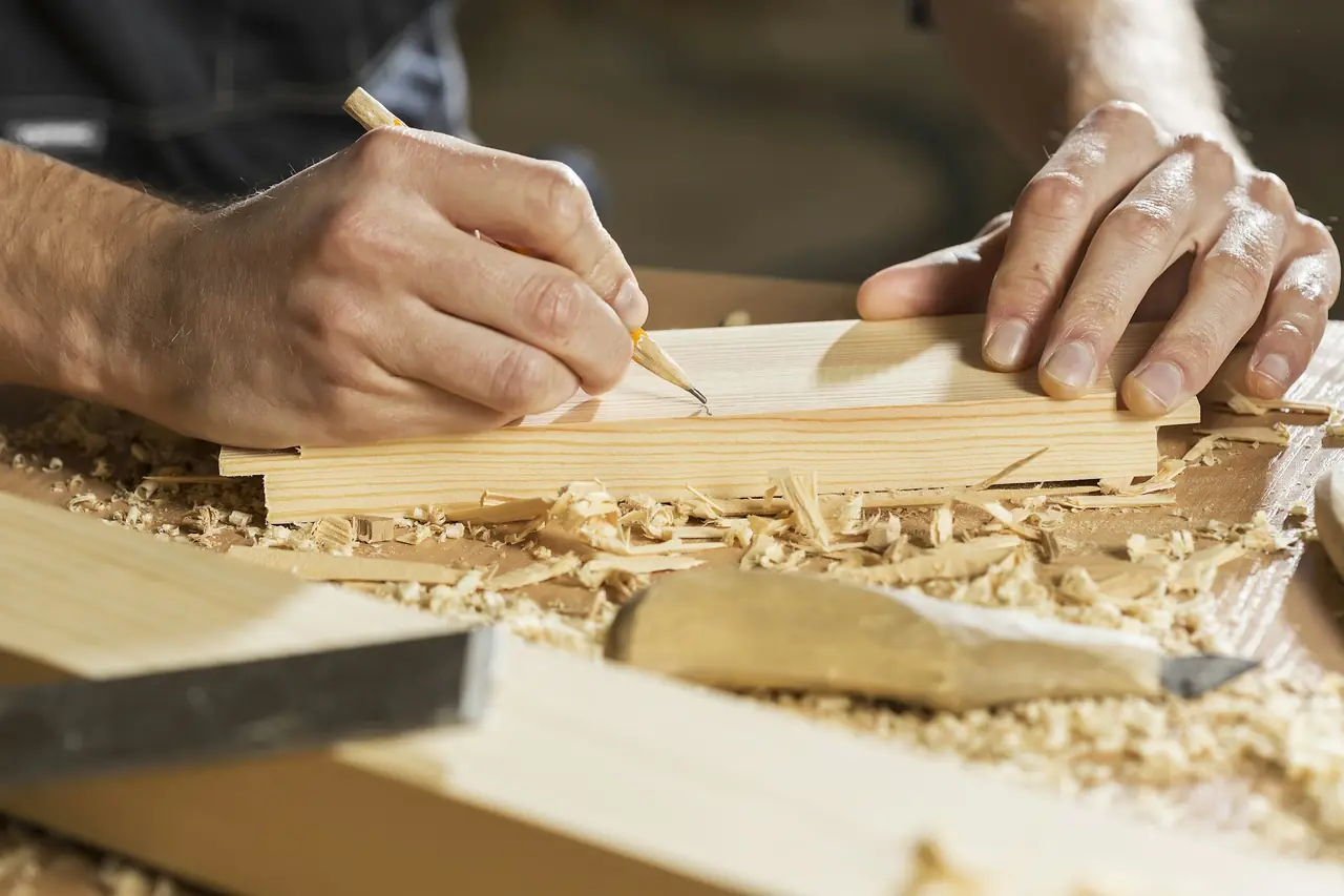 Menuisier traçant une coupe au crayon sur une planche, copeaux sur l'établi