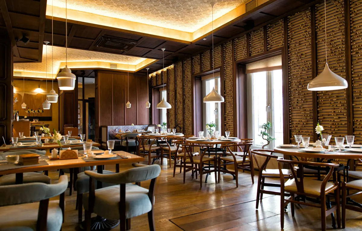 Salle du restaurant aux tables dressées, éclairée par des suspensions